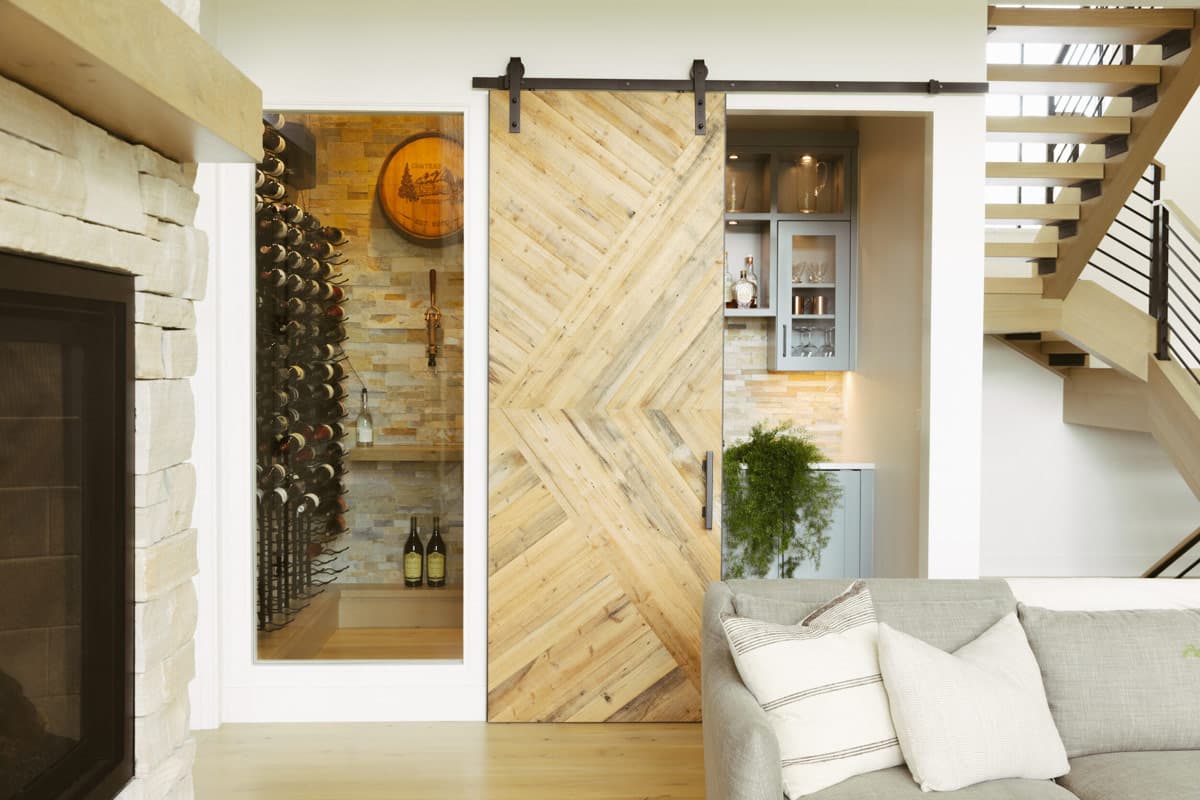 Interior view of a living area with stone fireplace, wine room, sliding barn door, and modern staircase.
