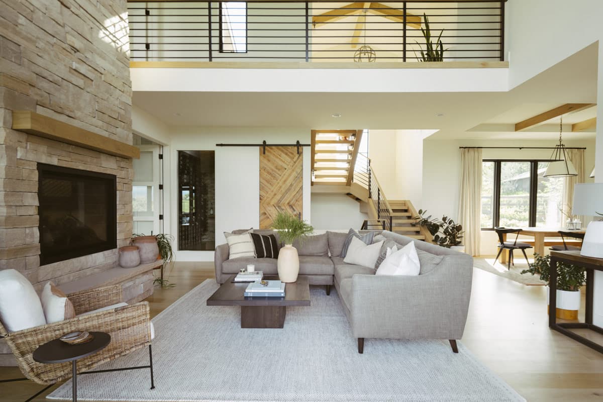 Open concept living room with stone fireplace, sectional sofa, wood barn door, and floating staircase with metal railing.