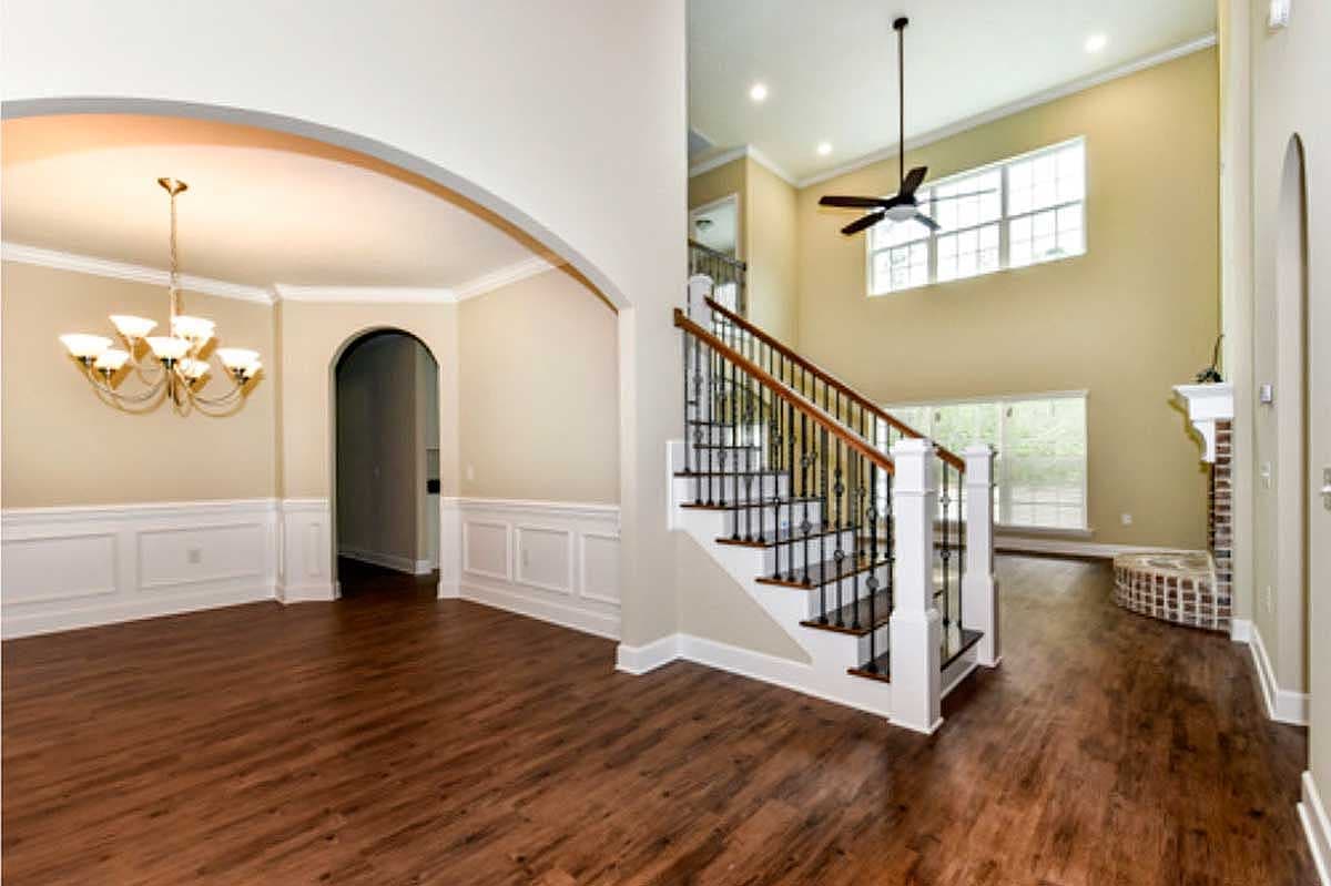 Interior view of a house showcasing a vaulted ceiling great room with a staircase, fireplace, and adjacent dining area with wainscoting.