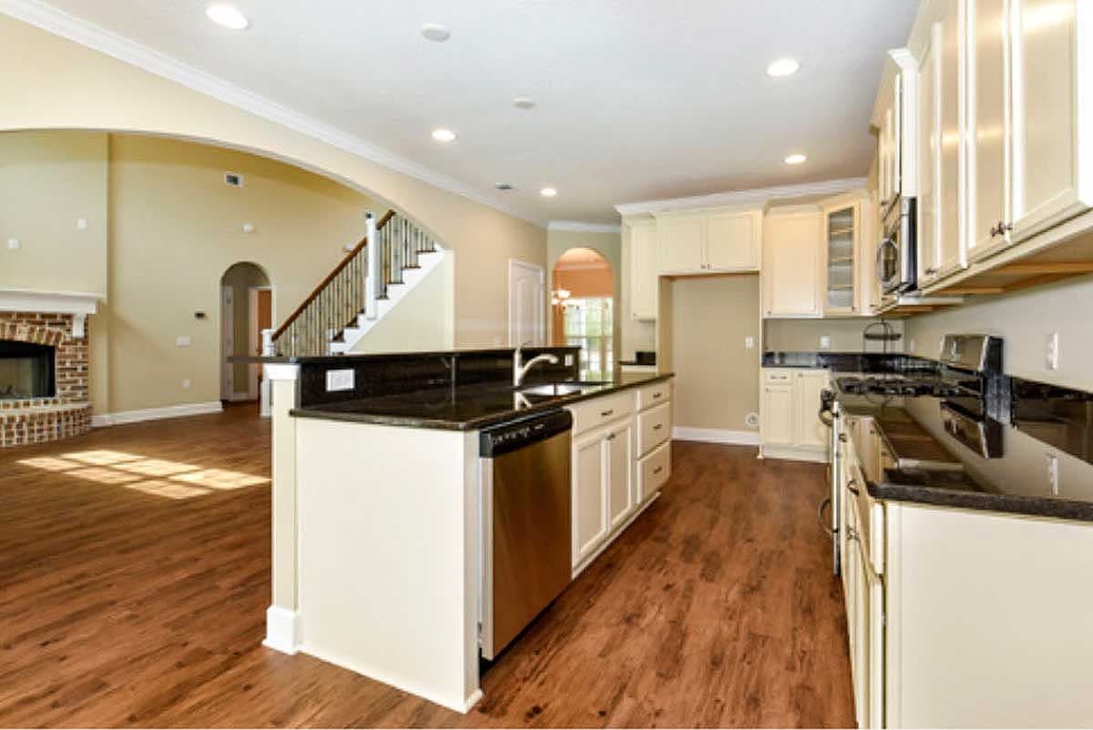 Open-concept interior featuring a kitchen island with sink, granite countertops, a brick fireplace, and a staircase.