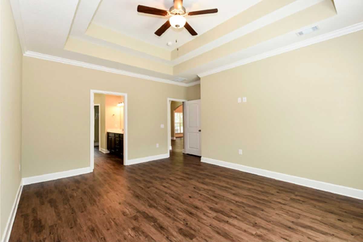 Interior view of a room with a tray ceiling, ceiling fan, wood flooring, and doorways to a bathroom and another room.