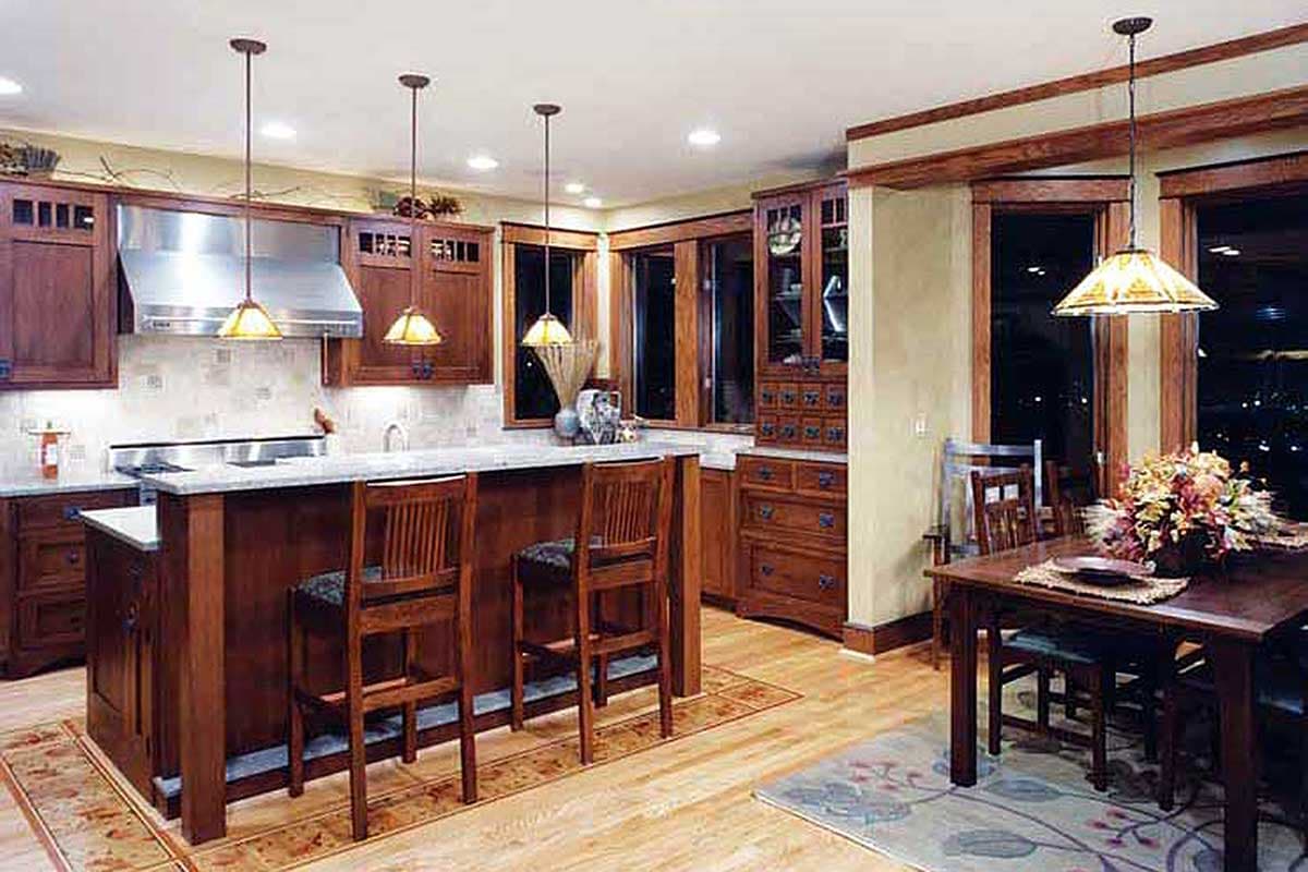 Kitchen with island seating, wood cabinetry, granite countertops, and dining area with wooden table and chairs.