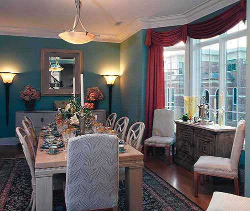 Formal dining room with a large table set for a meal, ornate sideboard, and windows with draped red curtains.
