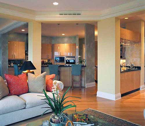 Open concept living area with kitchen island, bar stools, and cabinetry. Sofa in foreground.