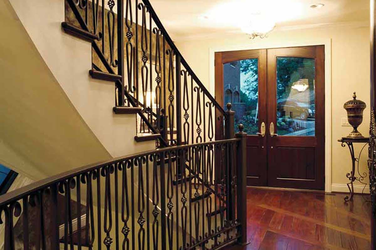 Interior view of a grand foyer with a curved staircase featuring ornate metal railings and double wooden doors.