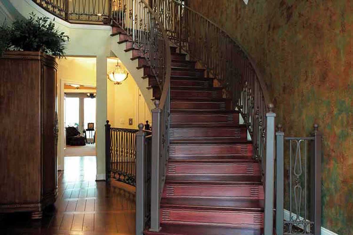 Curved staircase with dark wood treads and ornate metal balusters, flanked by decorative metal railing and textured wall.