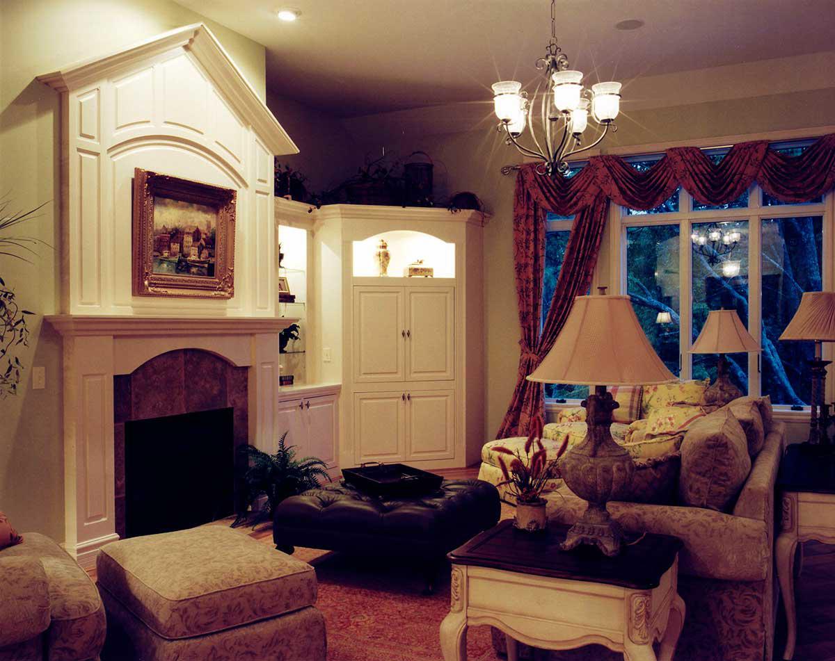 Living room with ornate fireplace, built-in cabinetry, plush seating, and large window overlooking trees.