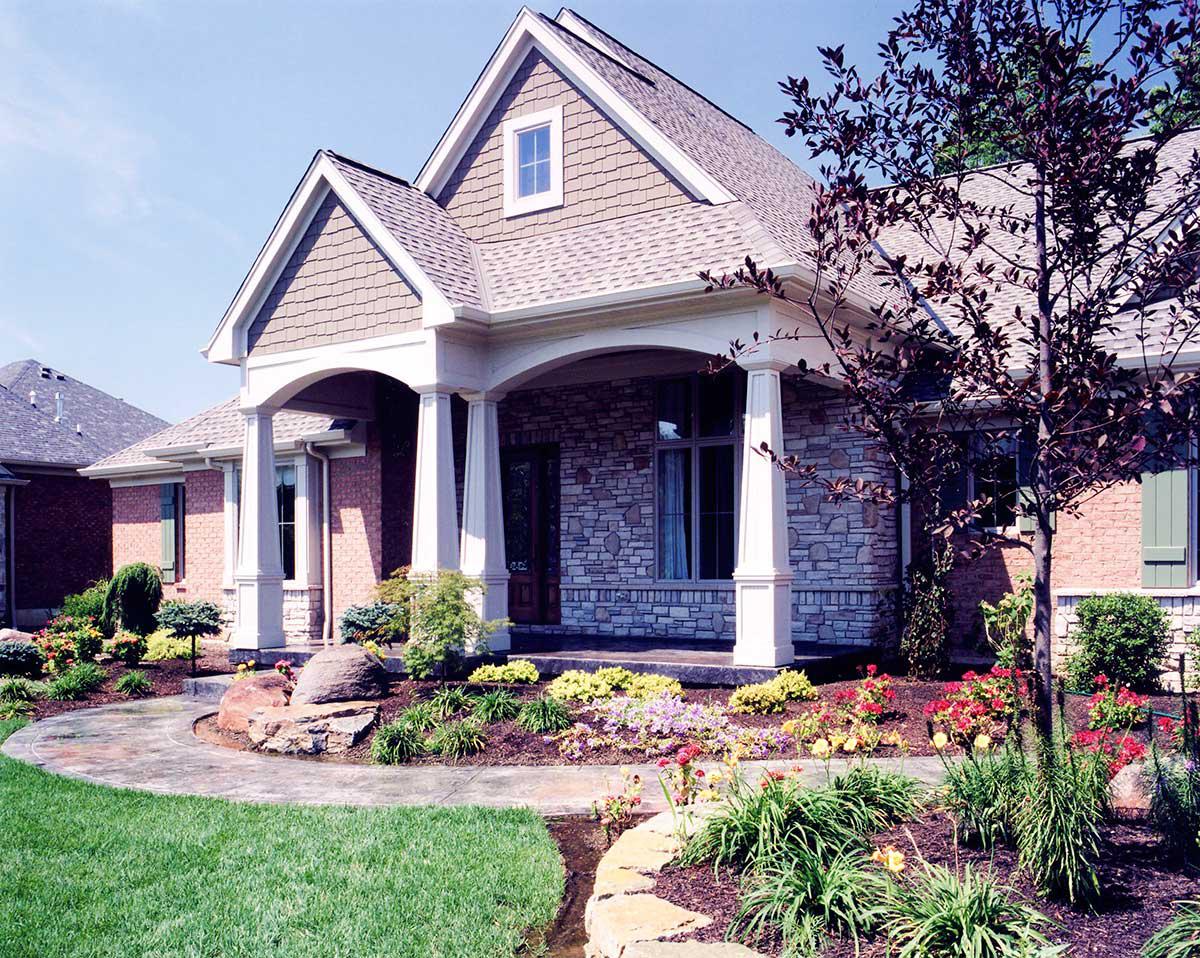 House plan exterior with stone and brick facade, arched covered porch with columns, and multiple gables.