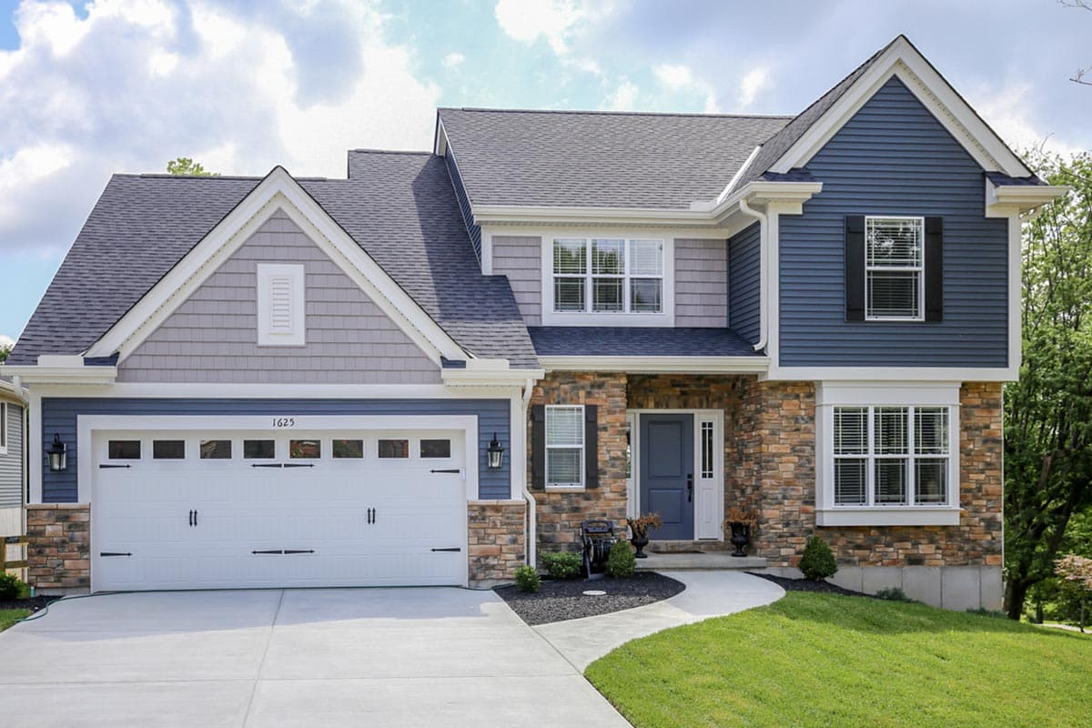 Two-story house plan exterior with stone and blue siding, a gable roof, and a white garage door.
