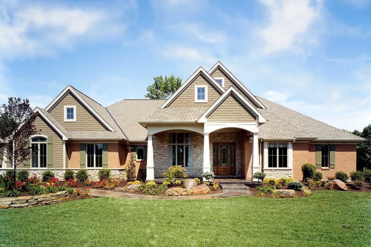 House plan exterior. One-story Ranch style home with gabled roof, covered porch with columns, and multiple dormers. Brick and stone facade.