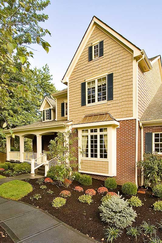 House plan exterior: Two-story home with shingle siding, brick base, wraparound porch, and bay window.