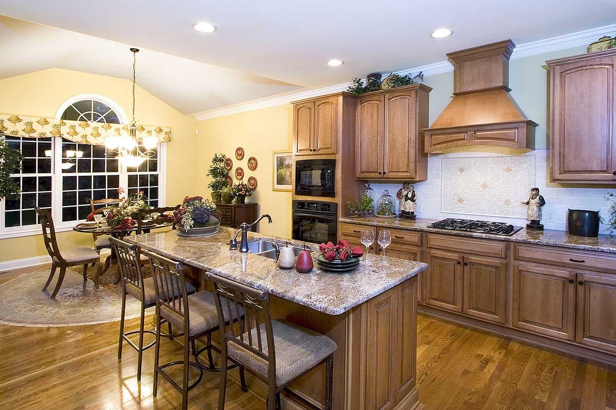 Kitchen with large island, granite countertops, double ovens, gas range, vaulted ceiling, and dining area with arched window.