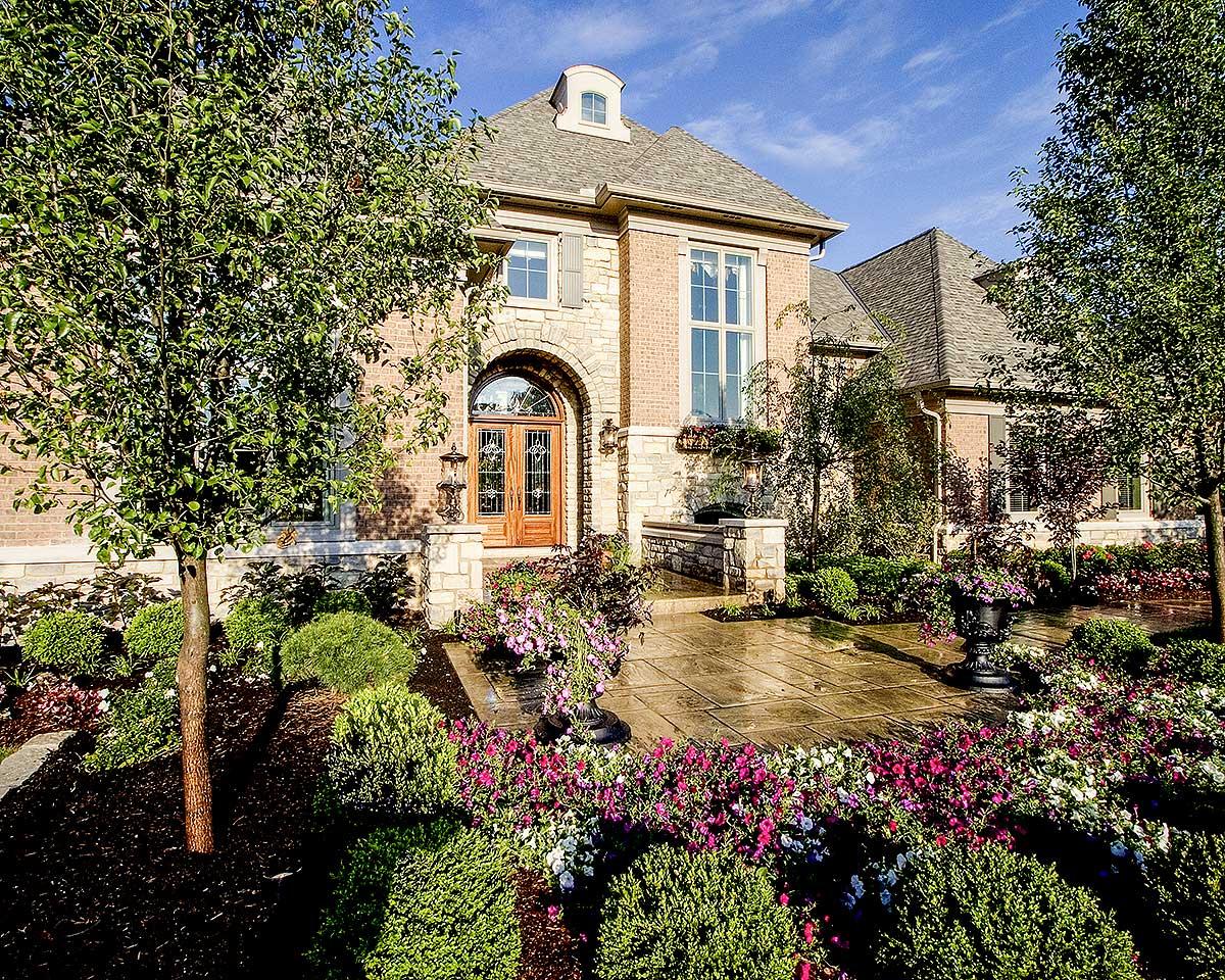House plan exterior: Brick two-story with arched entry, stone accents, multi-level roofline, and dormer.