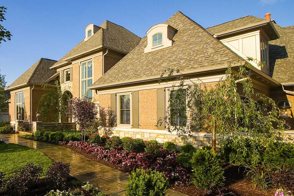 House plan exterior with brick facade, arched entryway, multiple gables, and arched dormer windows.
