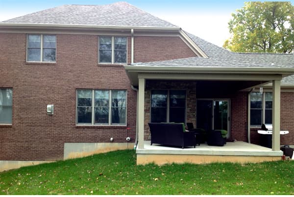 Two-story brick house exterior with covered patio, grill, and outdoor seating.