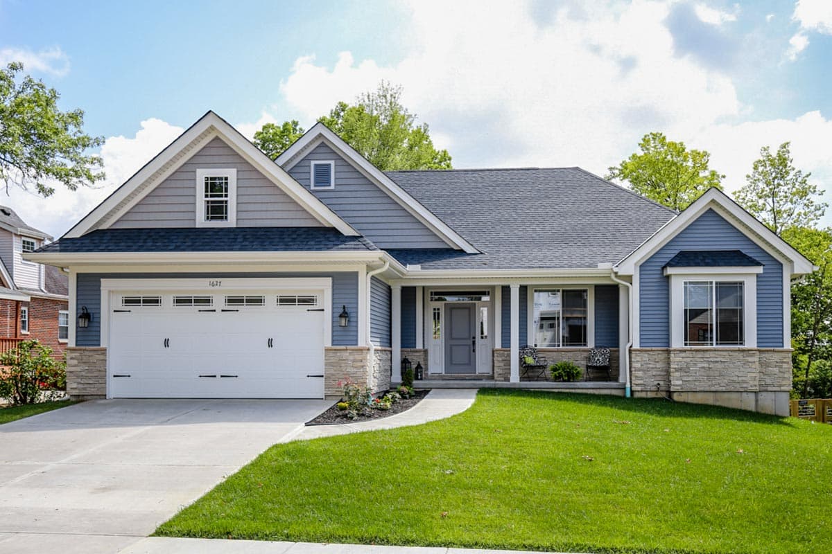 House plan exterior: Blue siding, stone accents, two-car garage, dormer window, covered entry with pillars.