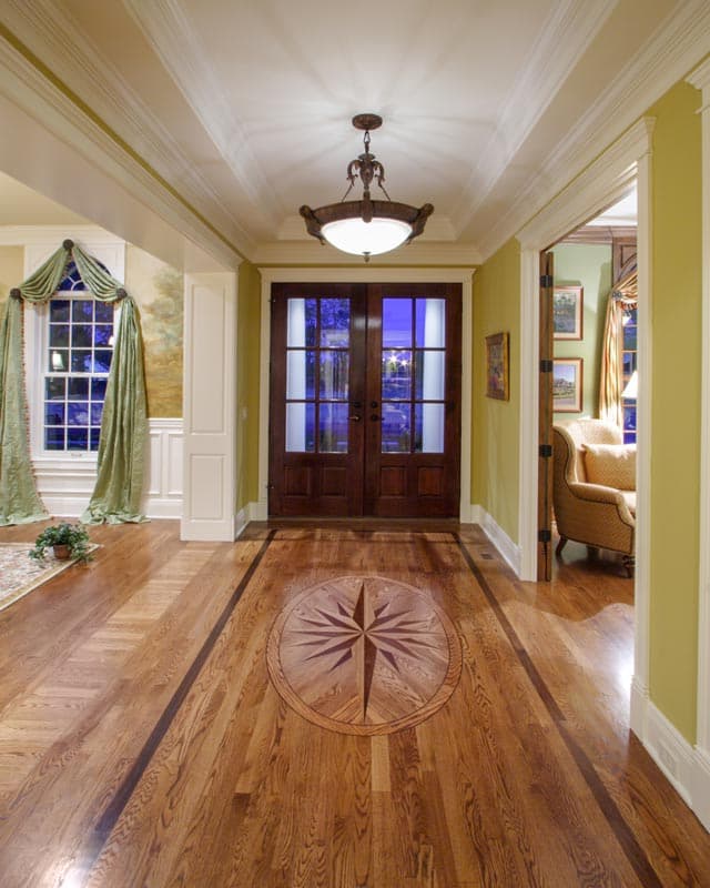 Entryway with double doors, decorative compass inlay floor, tray ceiling, and pendant light.