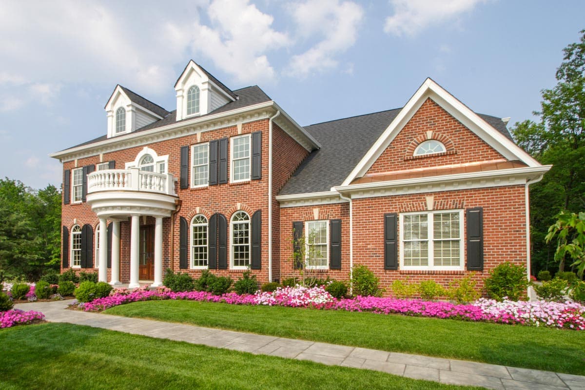 House plan exterior: Two-story brick home with curved balcony, columns, dormers, arched windows, and gables.