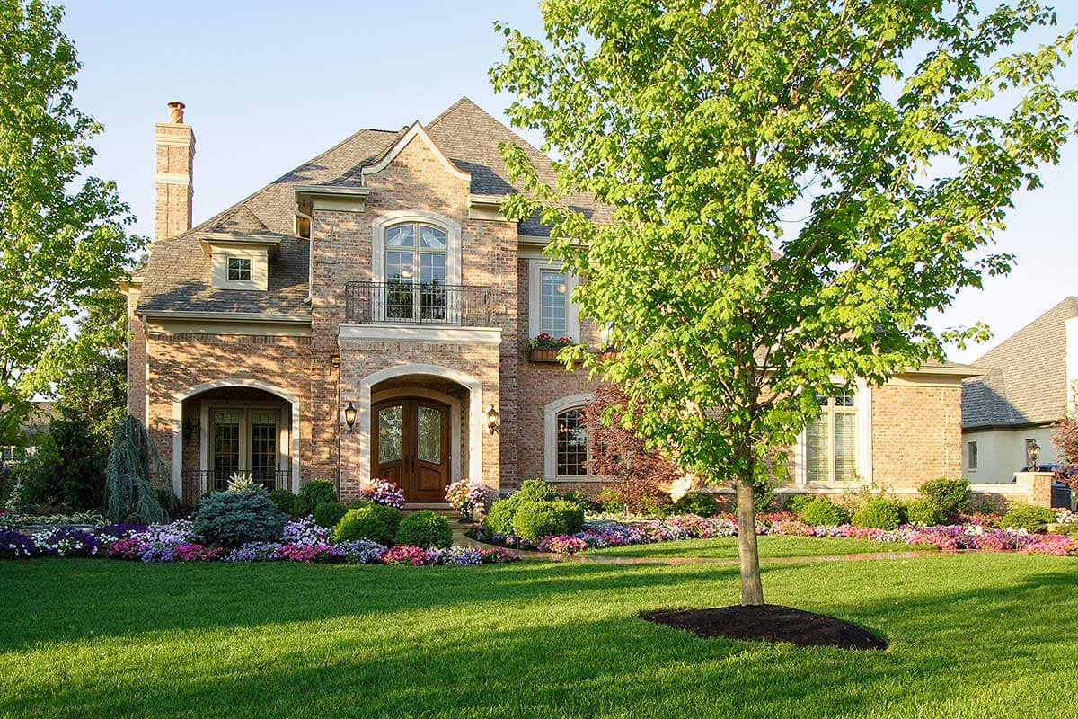 House plan exterior: Brick two-story home with arched entryway, dormers, gables, and a second-story balcony.