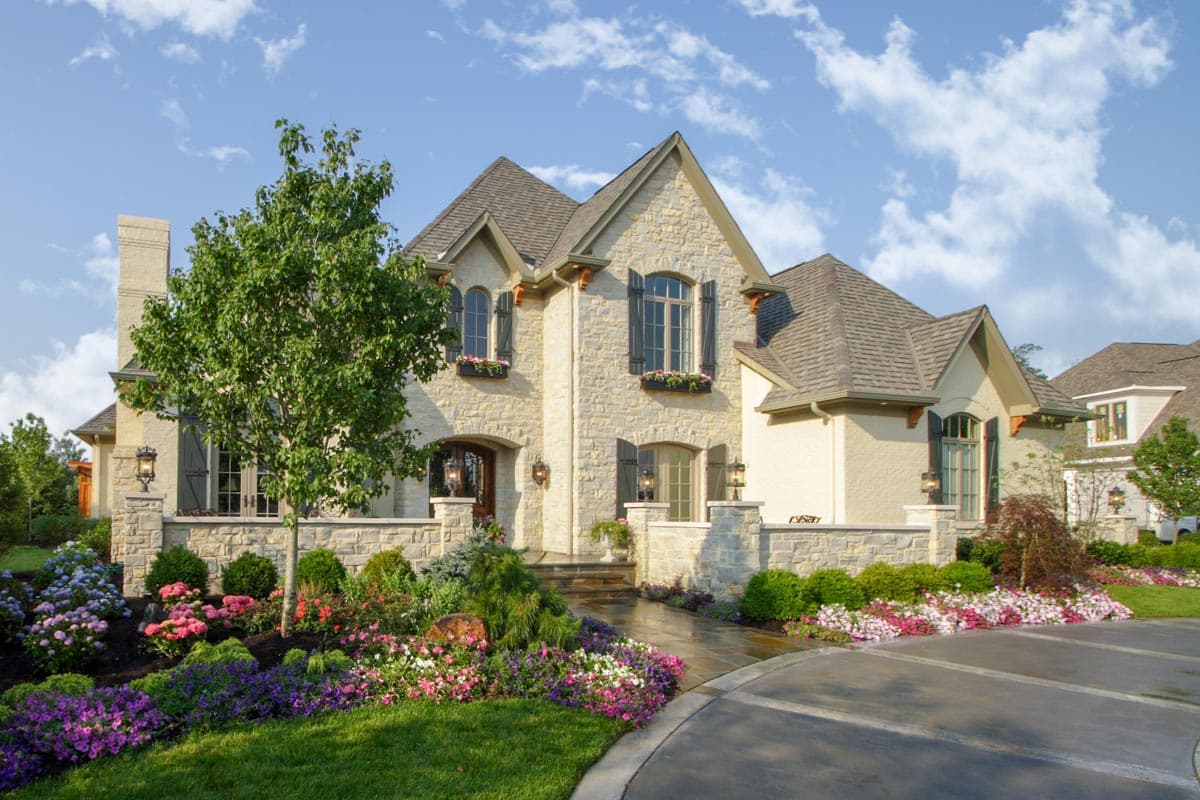 House plan exterior: Stone and stucco two-story home with gables, dormers, arched windows, and covered entry.
