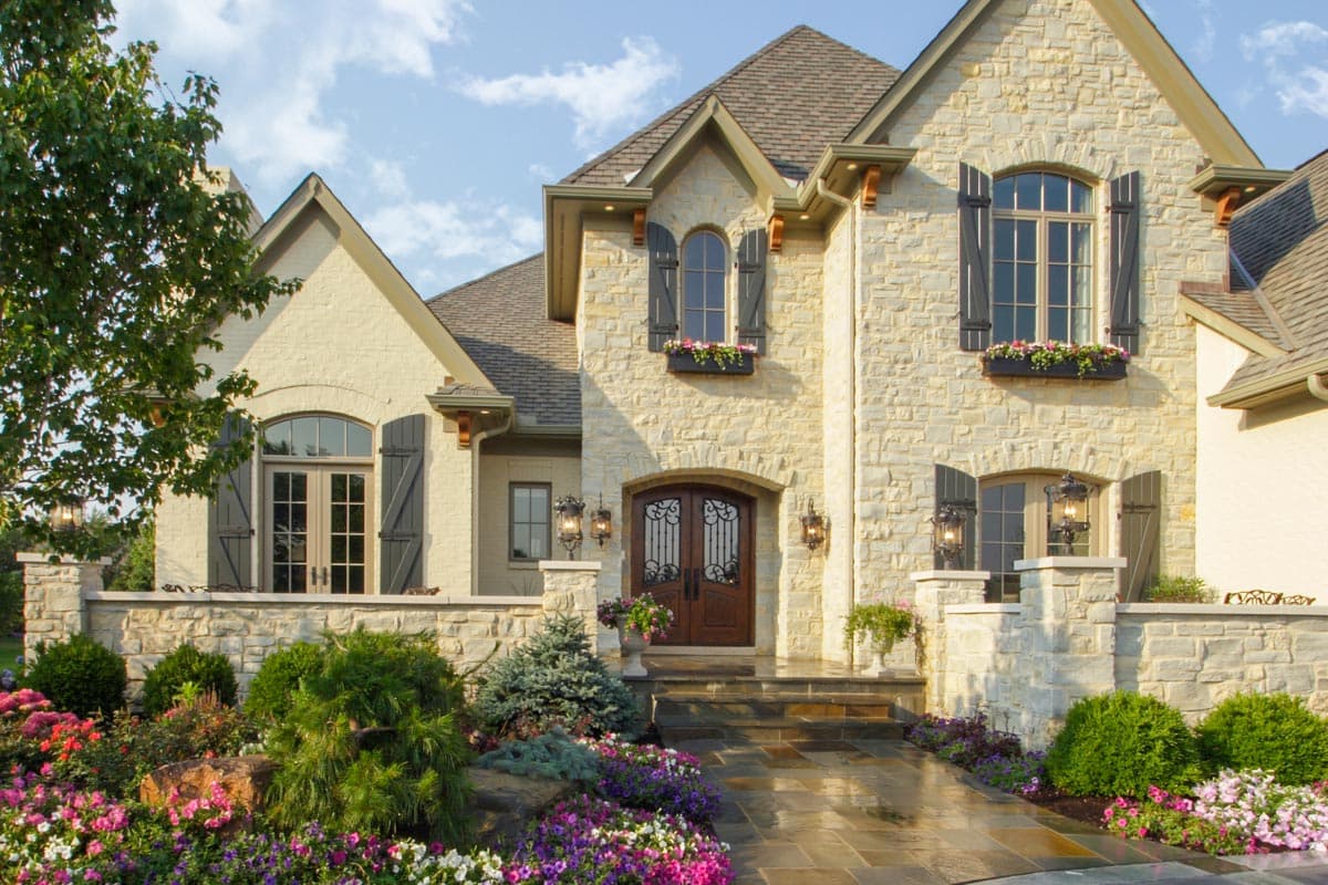 House plan exterior with stone facade, arched windows, dormers, and a prominent double door entry.