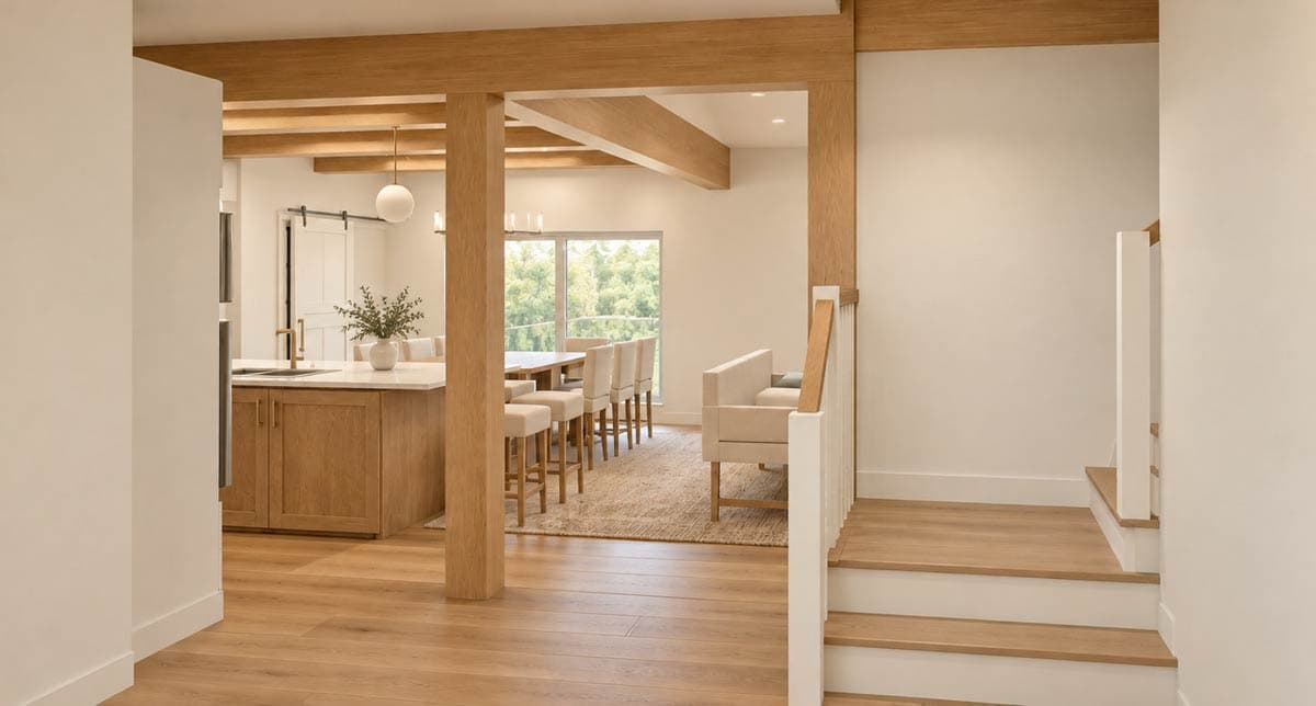 Interior view of an open-concept home with a kitchen island, dining area, and staircase, featuring exposed wood beams.