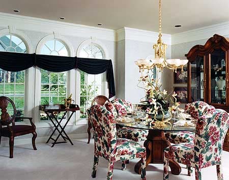 Dining room with glass top table, floral upholstered chairs, hutch, and bay windows with arched transoms.