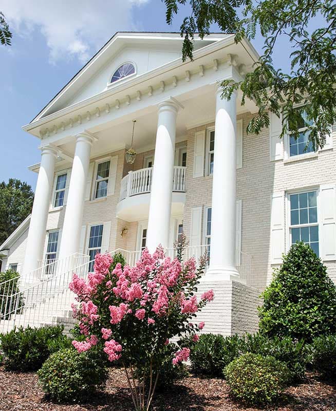 Neoclassical house plan exterior with portico, ionic columns, second-story balcony, and arched dormer window.