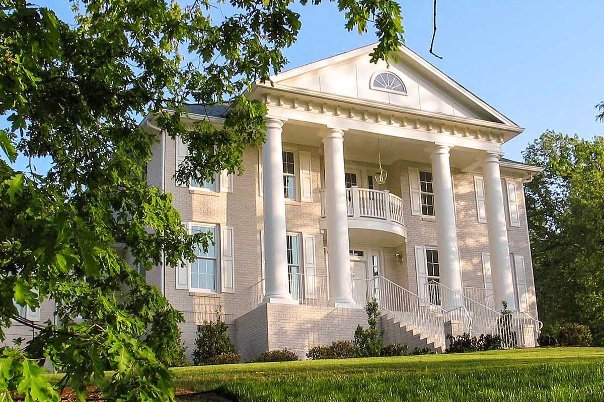 House plan exterior: Two-story neoclassical home with prominent columns, portico, balcony, and symmetrical window placement.