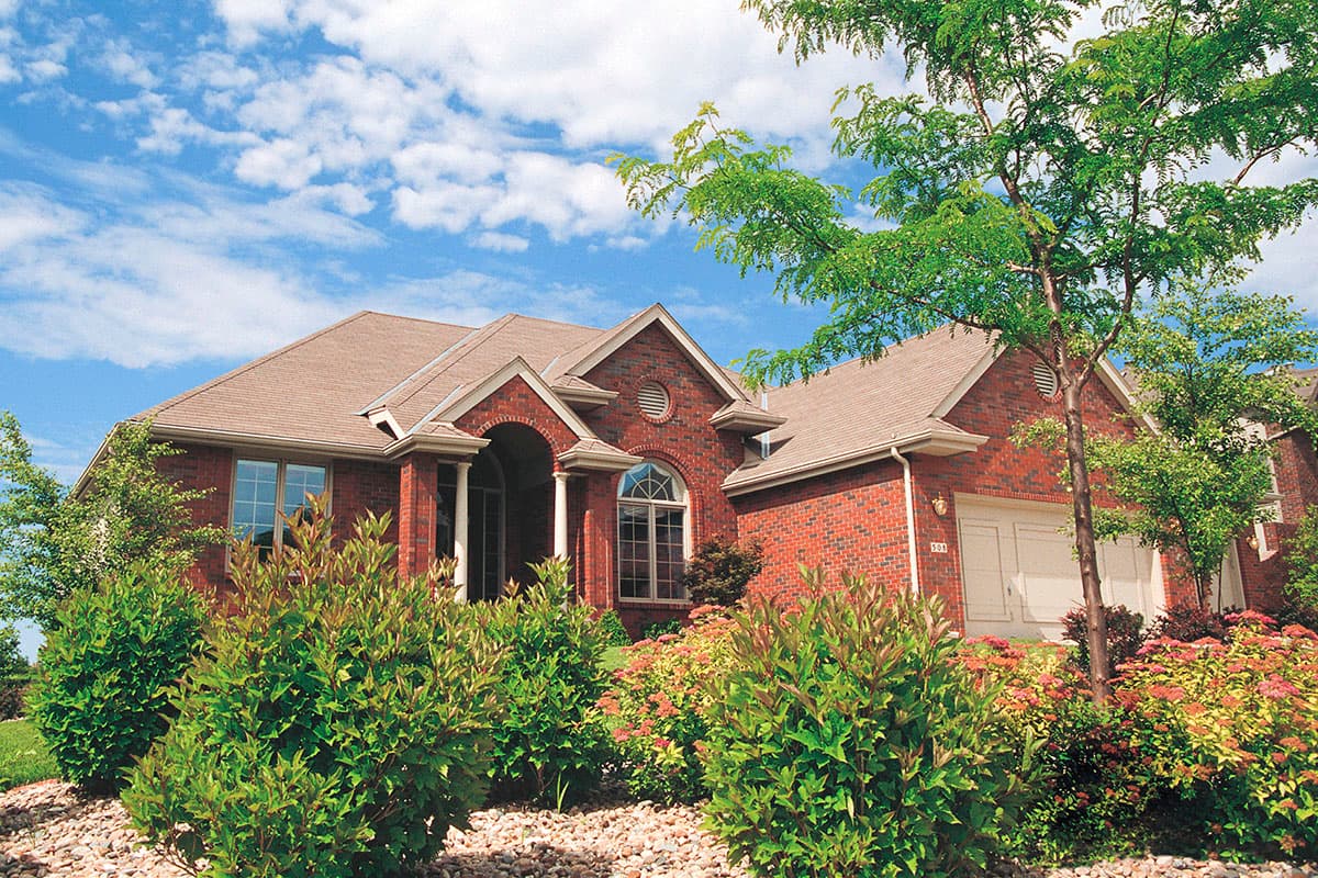 House plan exterior featuring a brick facade, arched portico with columns, gabled dormers, and a side-entry garage.