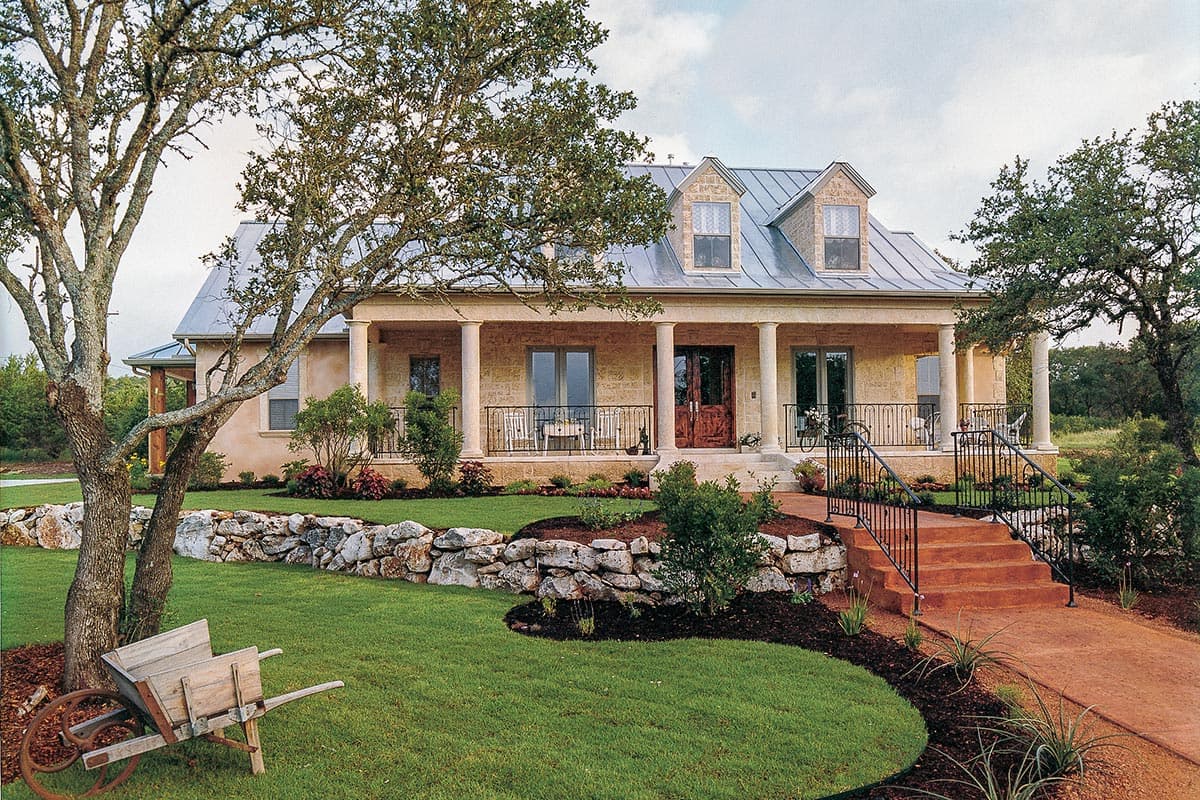 House plan exterior: Two-story stone home with metal roof, full-length porch with columns, and dormer windows.