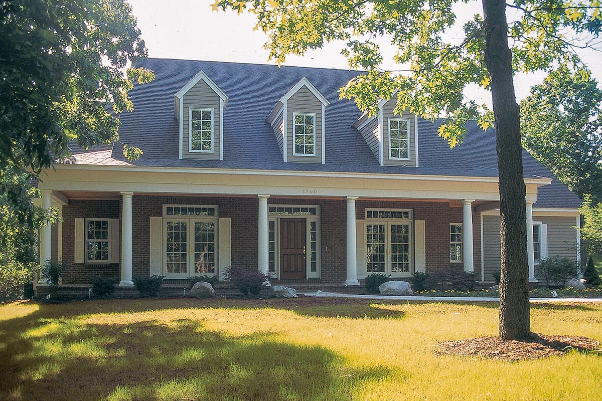 House plan exterior: Brick facade, full-width covered porch with columns, three dormer windows, and double entry doors.