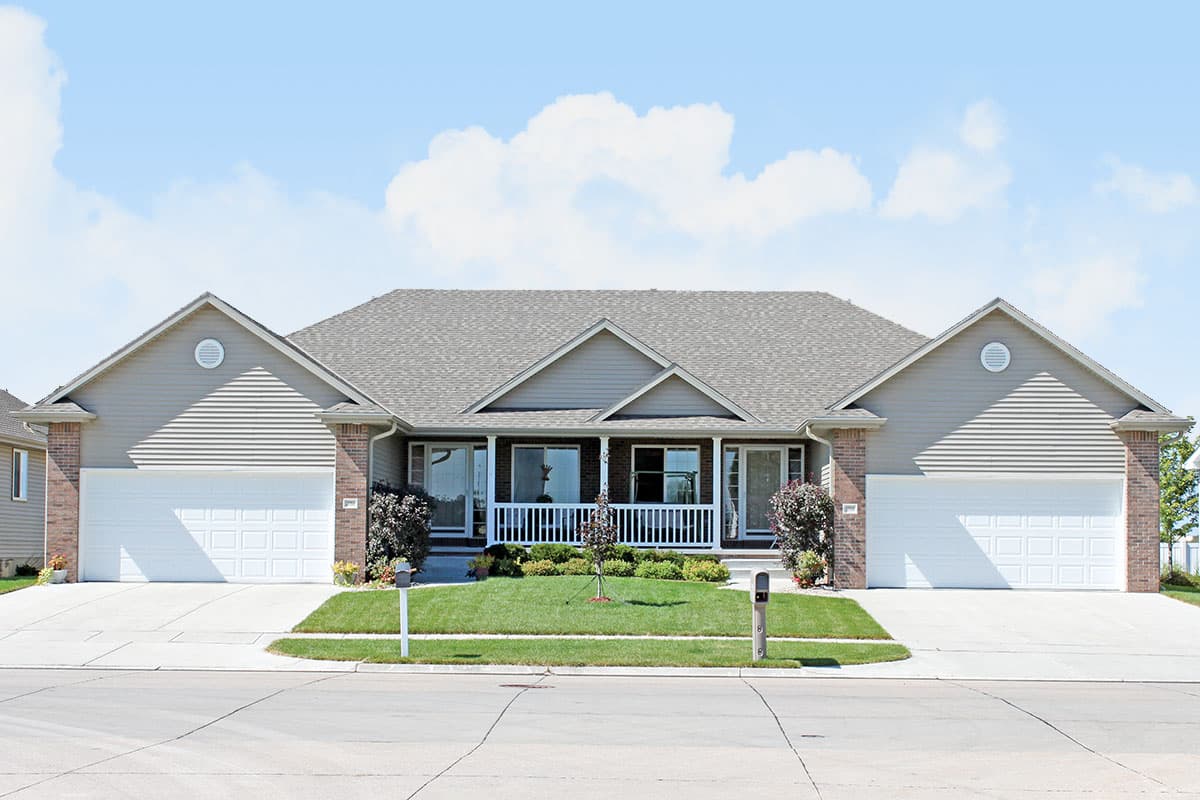House plan exterior of a one-story duplex with gable roofs, two attached garages, and a central covered porch with white railings.