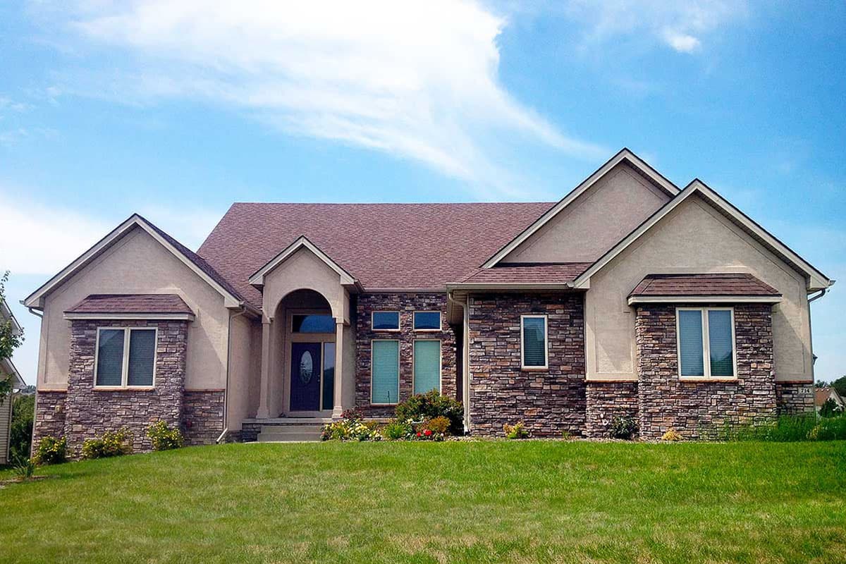 House plan exterior with stone veneer, arched entry, multiple gables, and varied rooflines.