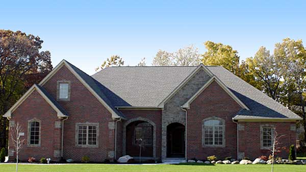 House plan exterior: Two-story brick home with stone accents, gables, dormers, and arched entryway.