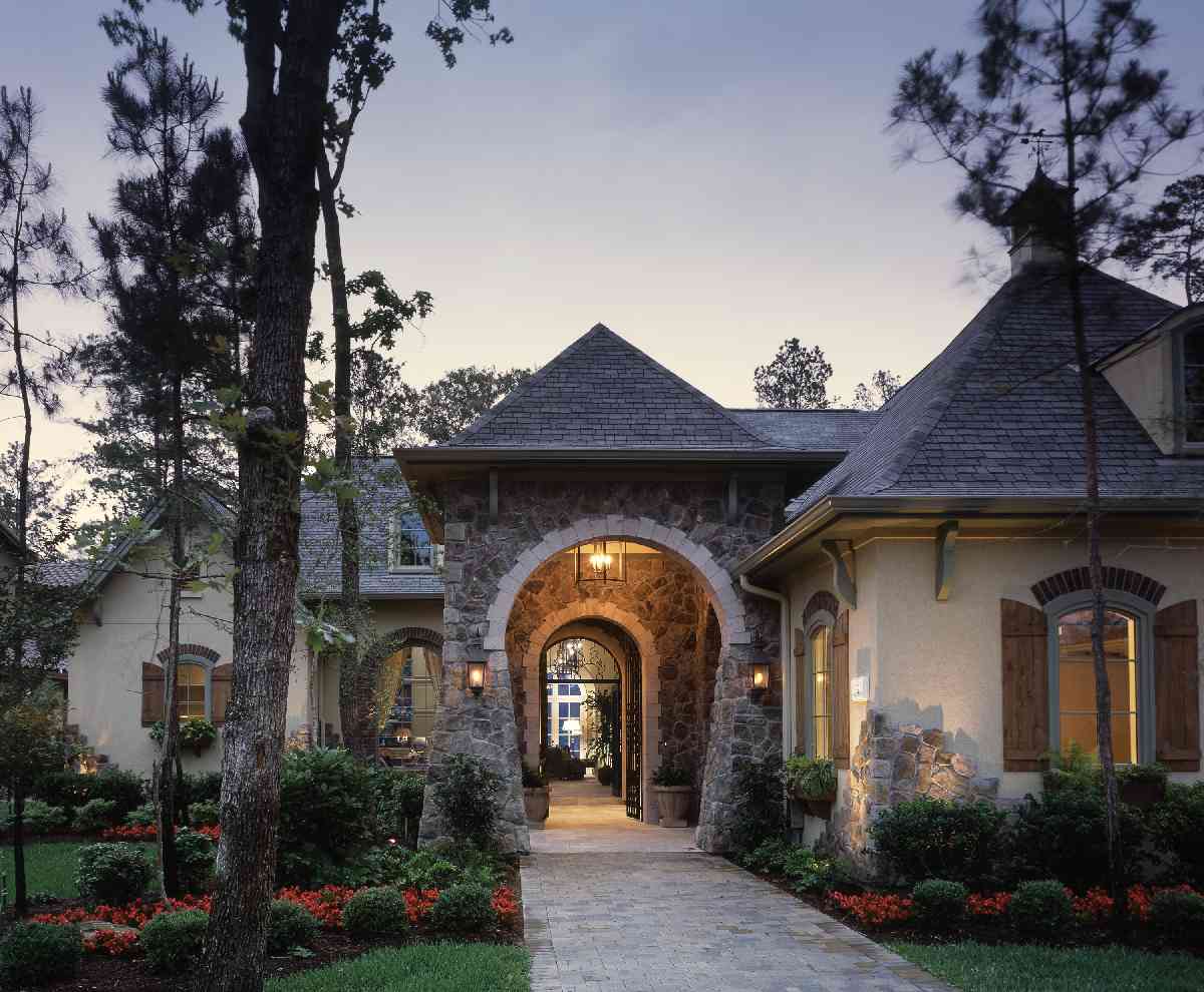 House plan exterior featuring stone archway entrance, multiple gables, and turreted rooflines with decorative shutters.
