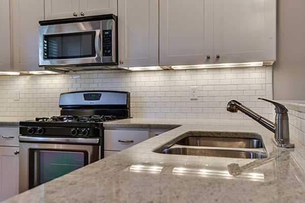 Kitchen area with stainless steel range, microwave, granite countertops, and subway tile backsplash.