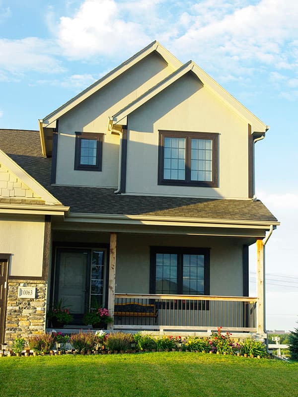 Two-story house plan exterior with stucco siding, gables, covered front porch with columns, and stone foundation.