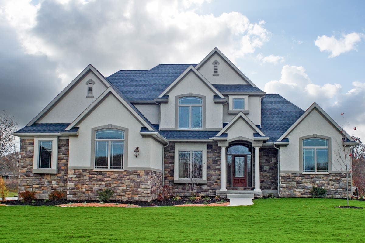 House plan exterior with stone accents, multiple gables, and a prominent front entry with columns. Two-story with arched windows.