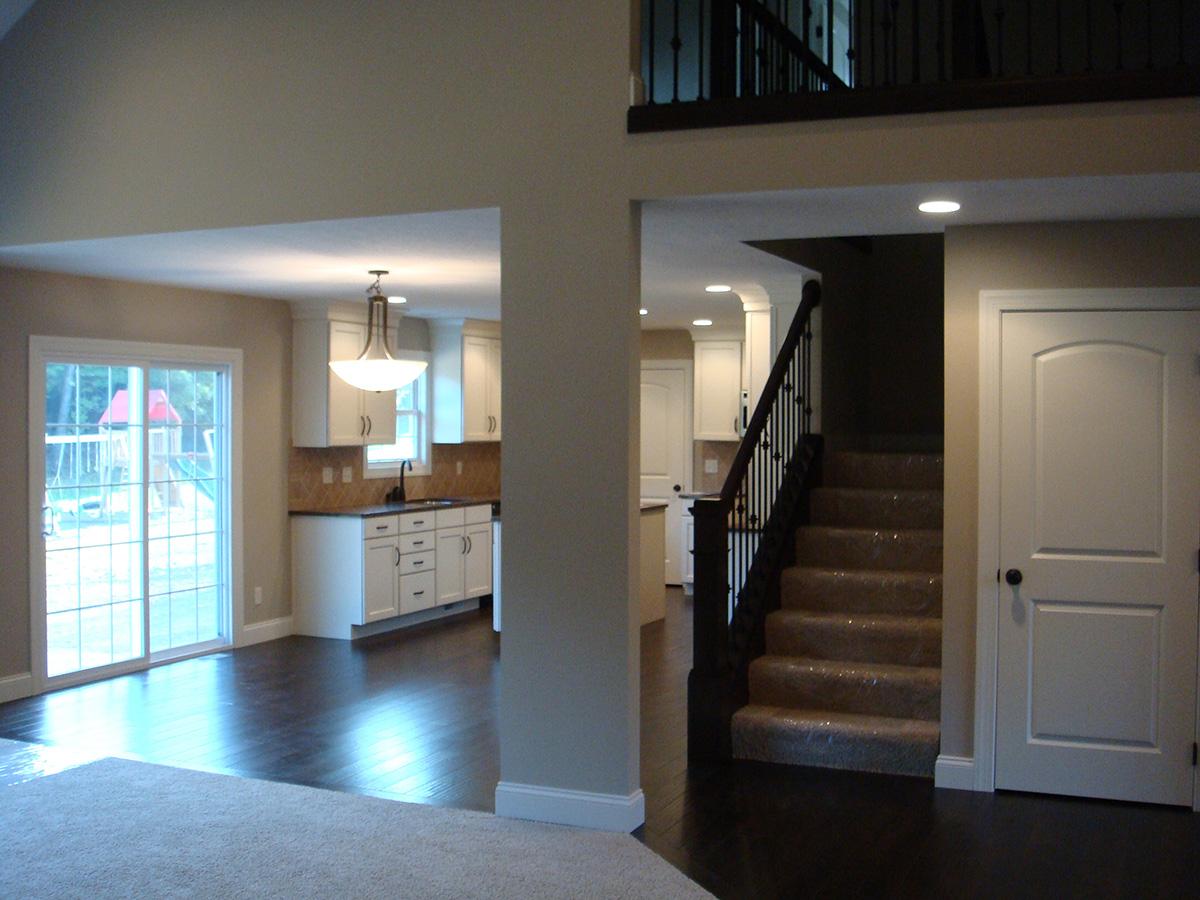 Open concept interior with a kitchen, white cabinetry, sliding glass doors, and a carpeted staircase with dark wood railing.