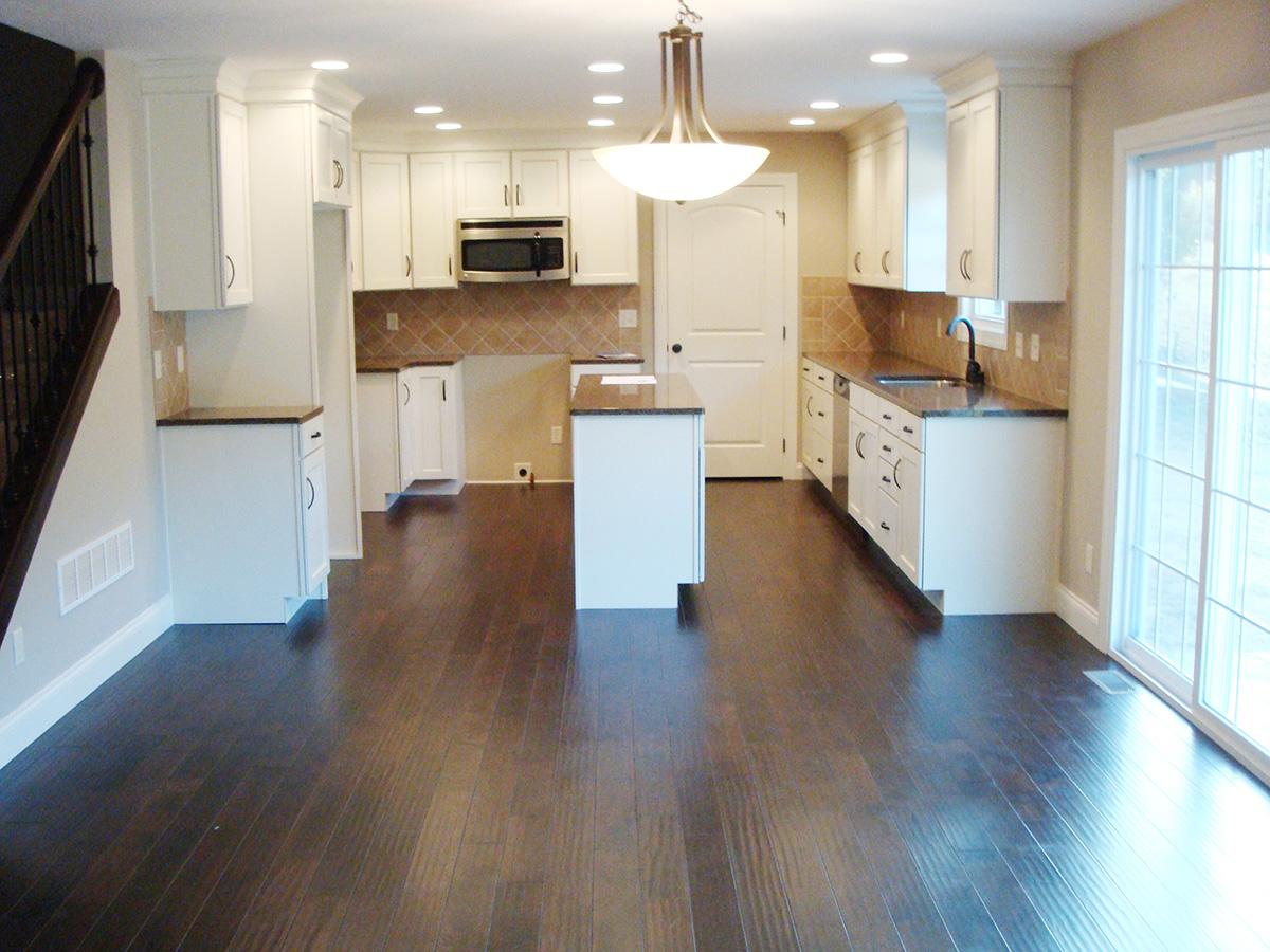 Interior view of a kitchen with white cabinets, a center island, dark wood floors, and a sliding glass door.