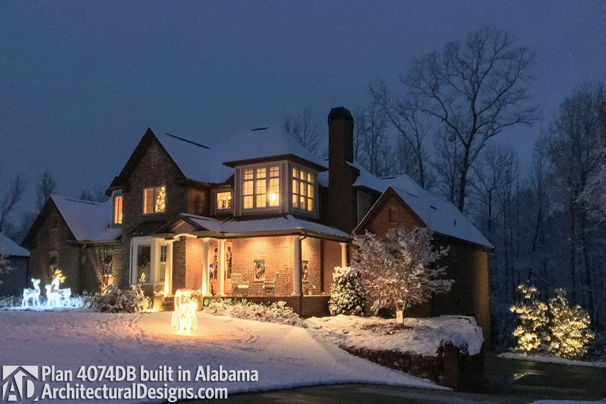 House plan exterior featuring a covered porch with columns, brick facade, dormers, and varied rooflines, seen in snow.