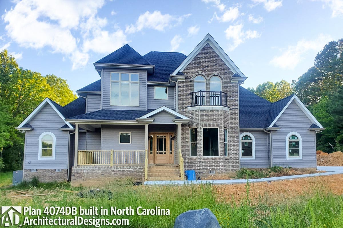 House plan exterior: Two-story home with gabled dormers, a prominent brick facade, second-story balcony, and covered front porch.