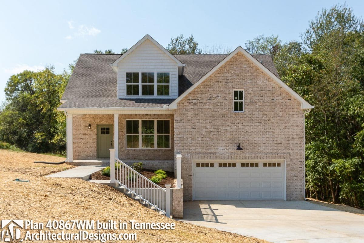 House plan exterior: Two-story brick home with front porch, dormer, gabled roof, and attached garage.