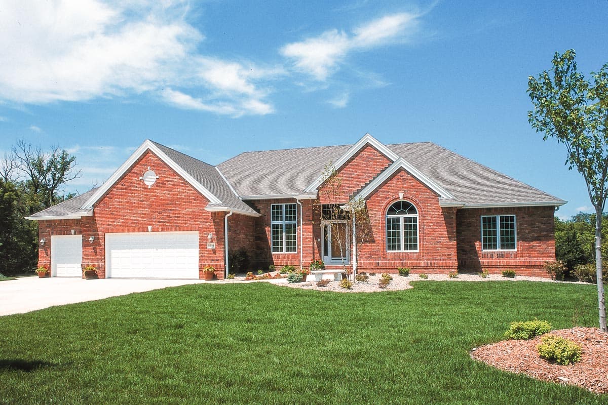 House plan exterior: Brick ranch with a prominent front gable, two-car garage, and arched entry window.