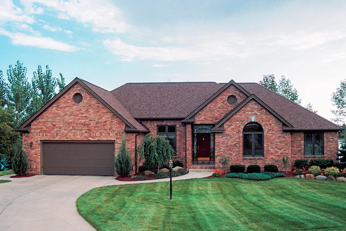 House plan exterior: Red brick ranch with attached garage, multiple gables, and arched windows.