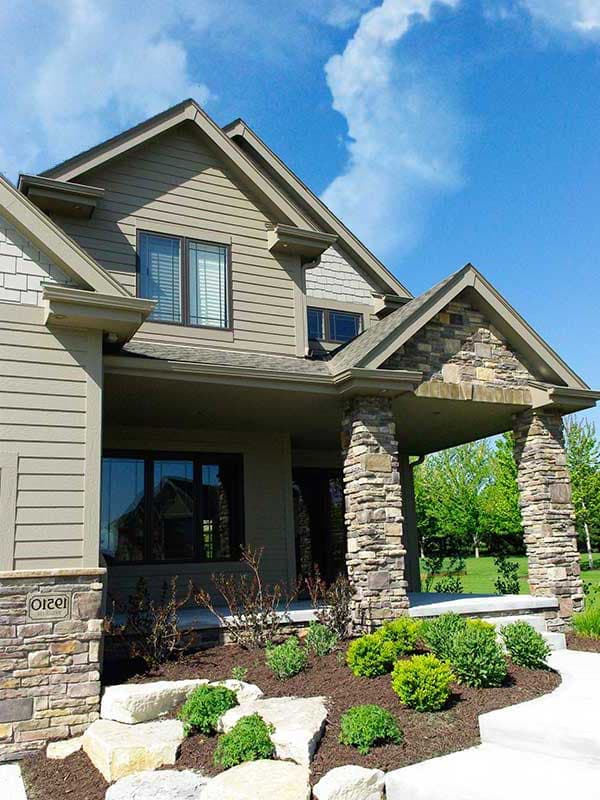 House plan exterior: Two-story home with stone-clad porch columns, gables, and siding.