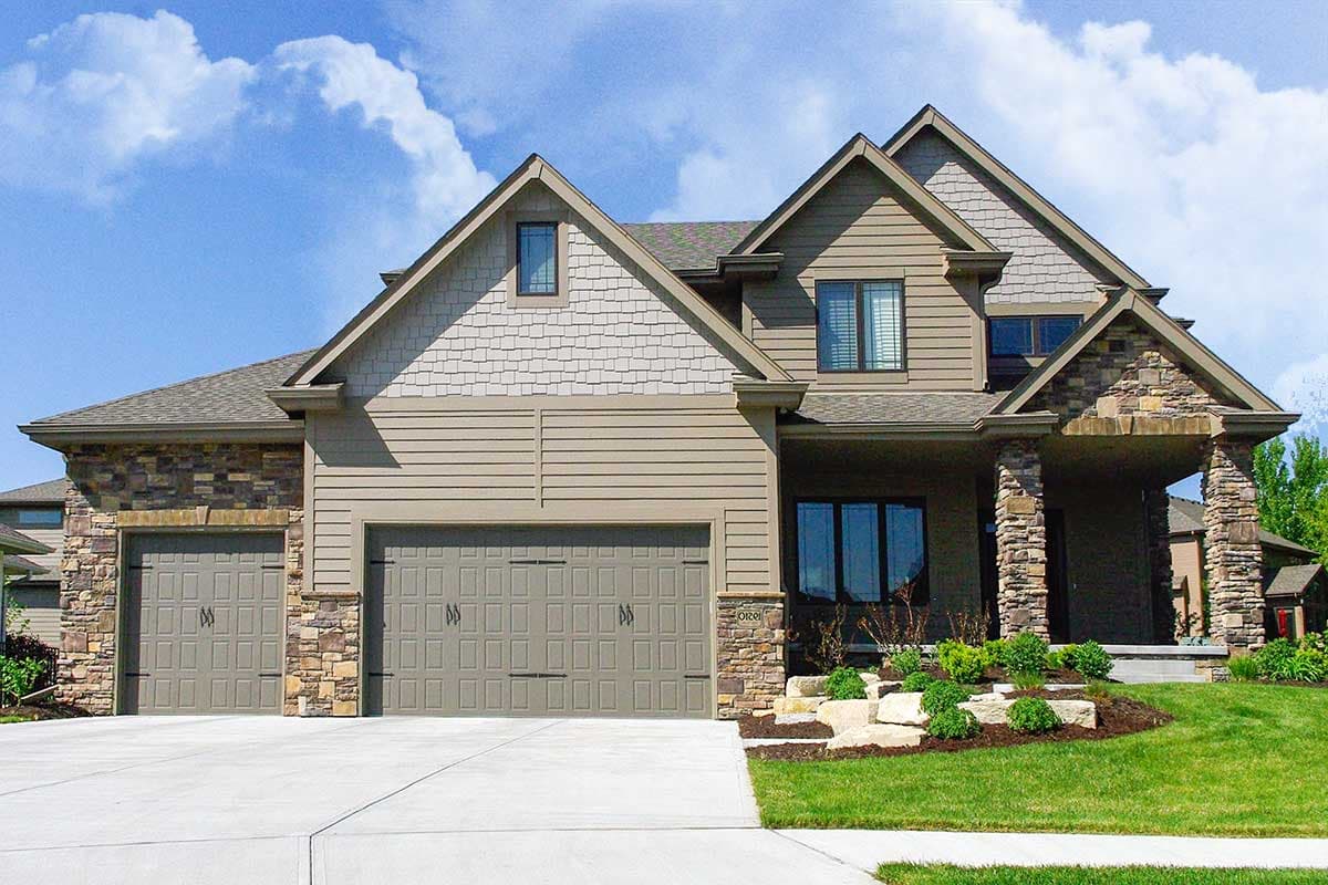 Two-story house plan exterior with a three-car garage, stone accents, gable dormers, and covered porch.
