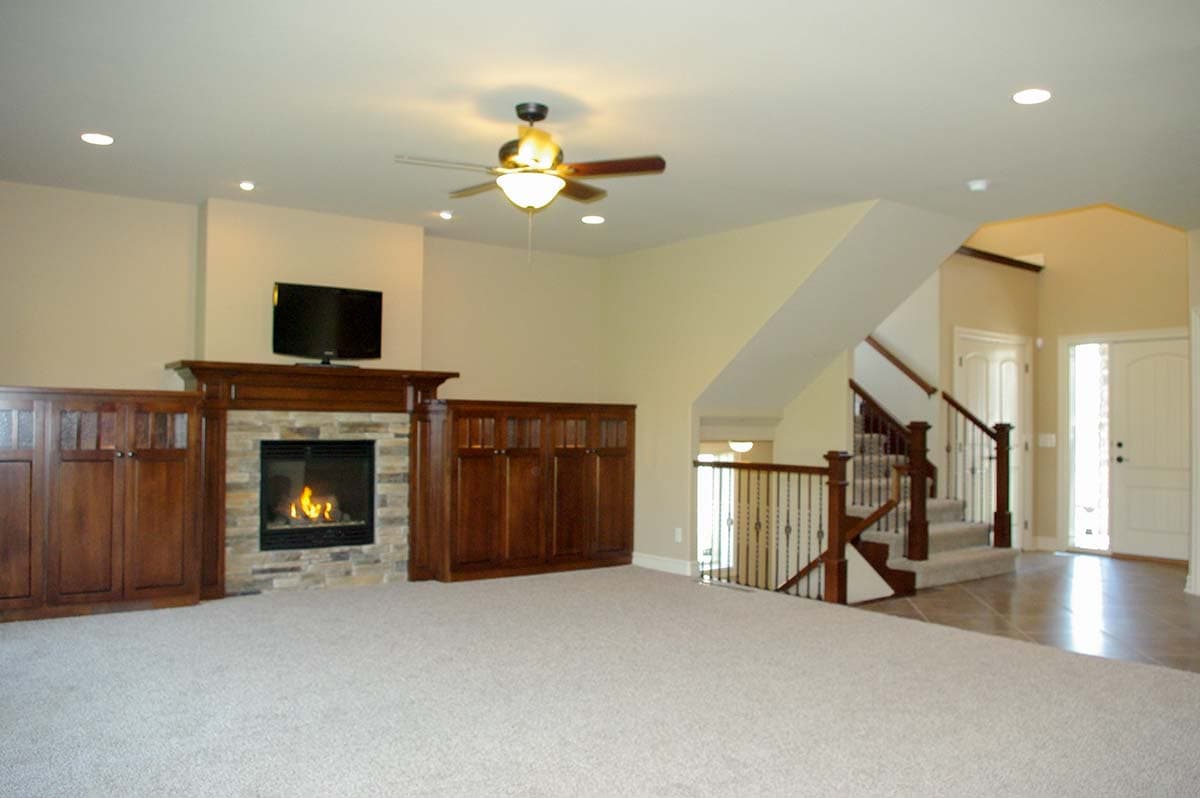 Interior view of living room with stone fireplace, built-in cabinetry, and staircase leading to upper level.