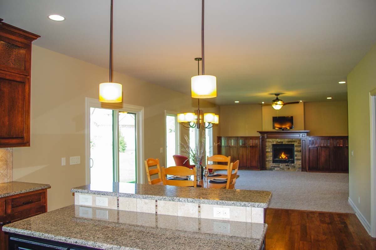 Open concept living area with kitchen island, dining space, and living room featuring stone fireplace and built-in cabinetry.